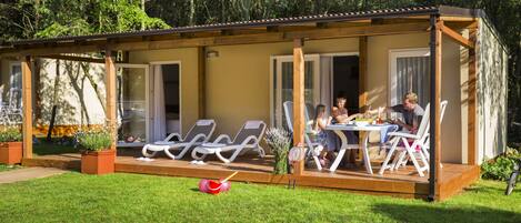 A covered outdoor dining area with a table and chairs, surrounded by a wooden deck and glass doors.