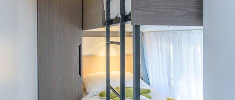 Una cama individual superpuesta con un armario de madera y un peluche en la cama inferior.