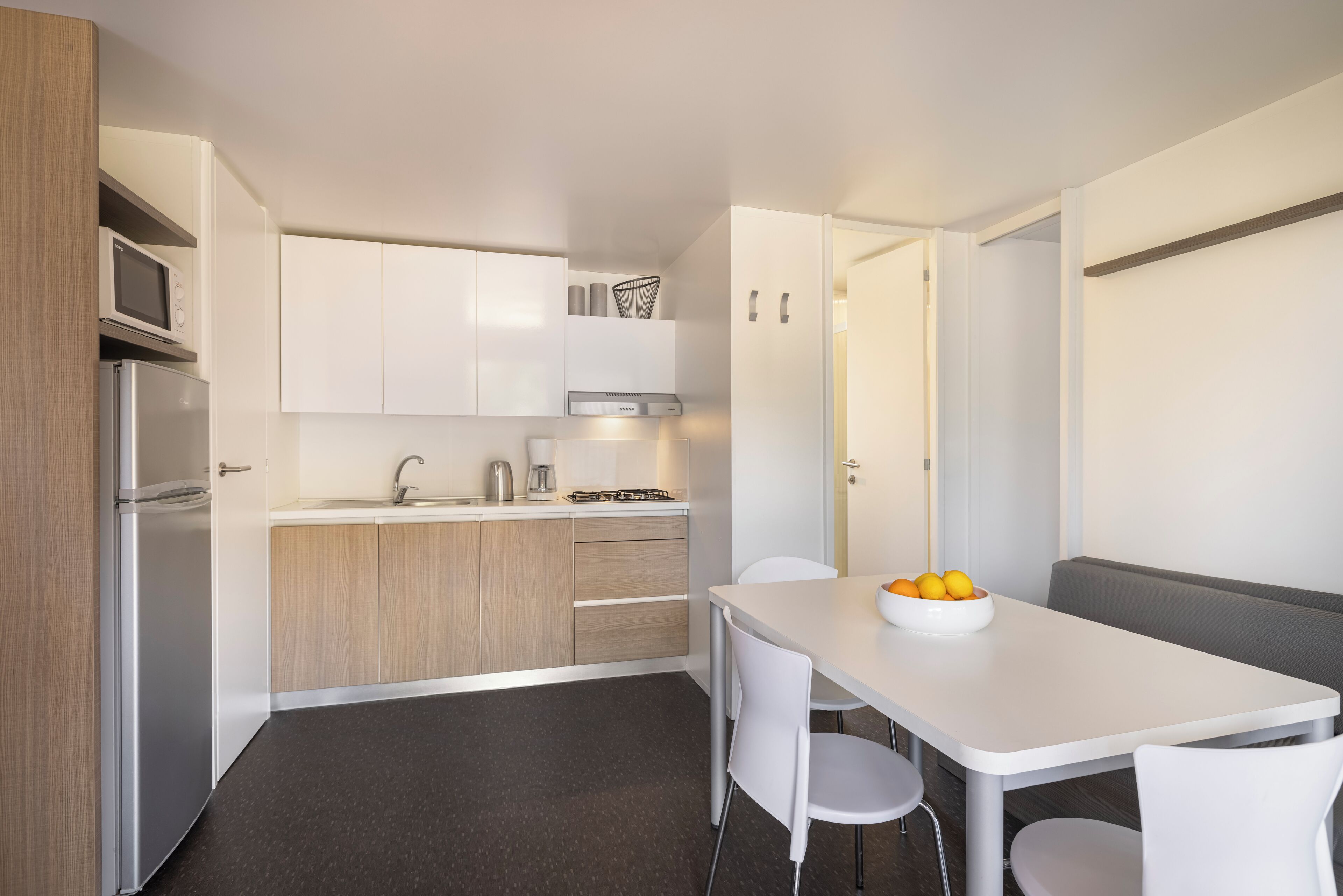 Une cuisine moderne avec des armoires blanches, un réfrigérateur en acier inoxydable, un four à micro-ondes et une cuisinière à gaz. On y trouve une table à manger avec des chaises blanches et un saladier de fruits posé dessus.