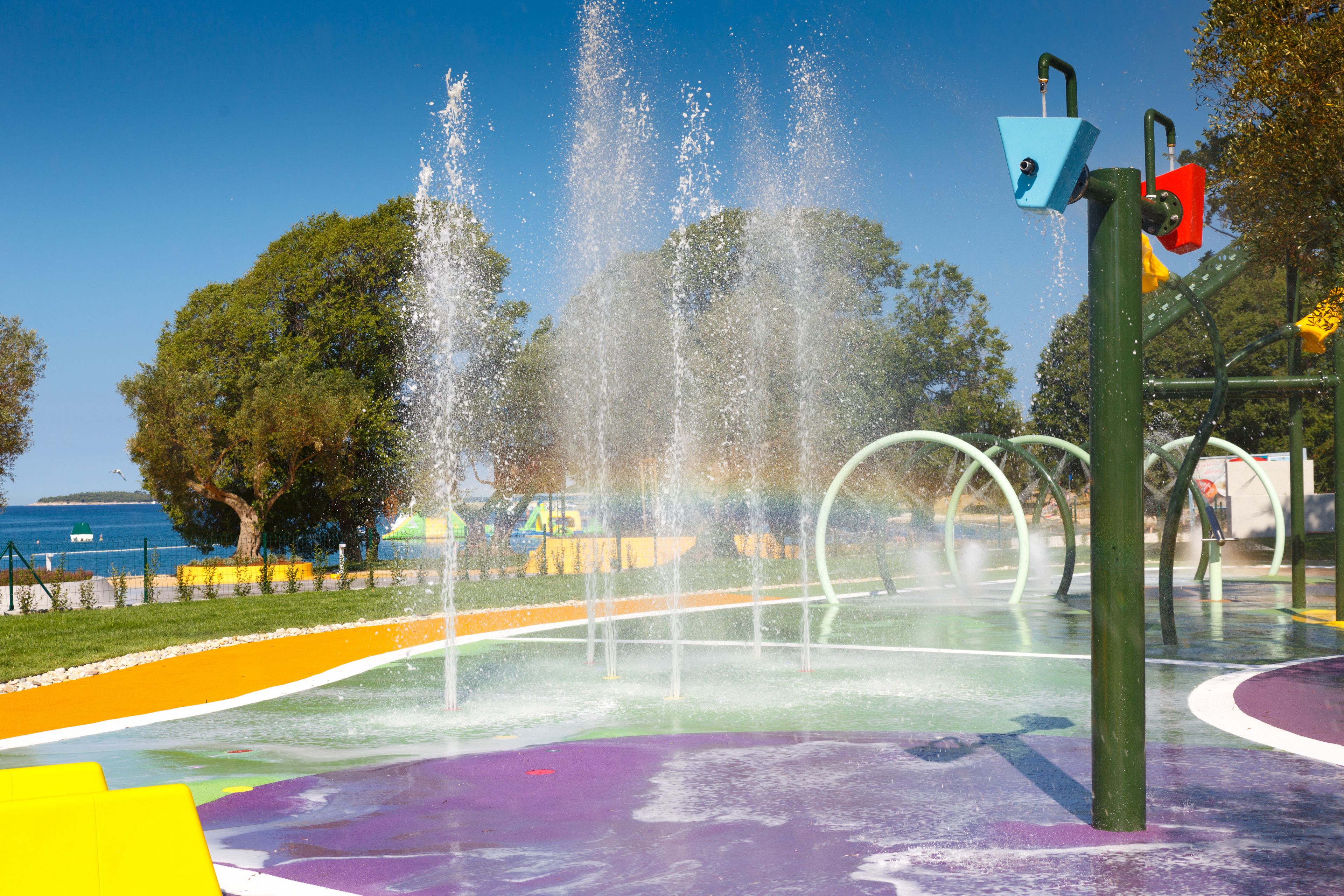 Un espace de jeux aquatiques doté de plusieurs fontaines et d’une surface au sol aux couleurs vives.