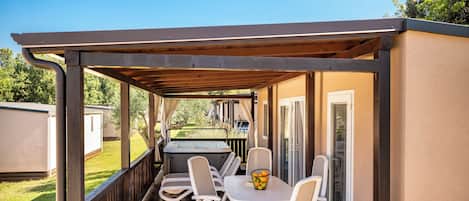 A covered patio with a table and chairs, a hot tub, and a view of a backyard.