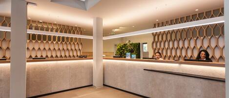 A modern reception area with a geometric patterned wall, a reception desk, and a potted plant.