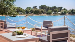 A seaside terrace with outdoor seating, a table with a notebook and a basket of fruit, and a view of the sea and trees. - Maistra Camping Polari Mobile homes   (Rovinj)