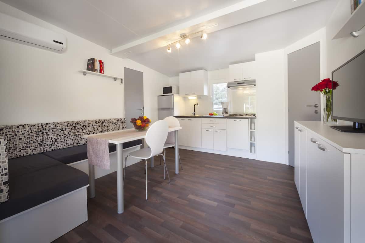 Une cuisine moderne avec des meubles blancs, un coin repas doté d’une table et de chaises blanches, et un canapé aux motifs noir et blanc.