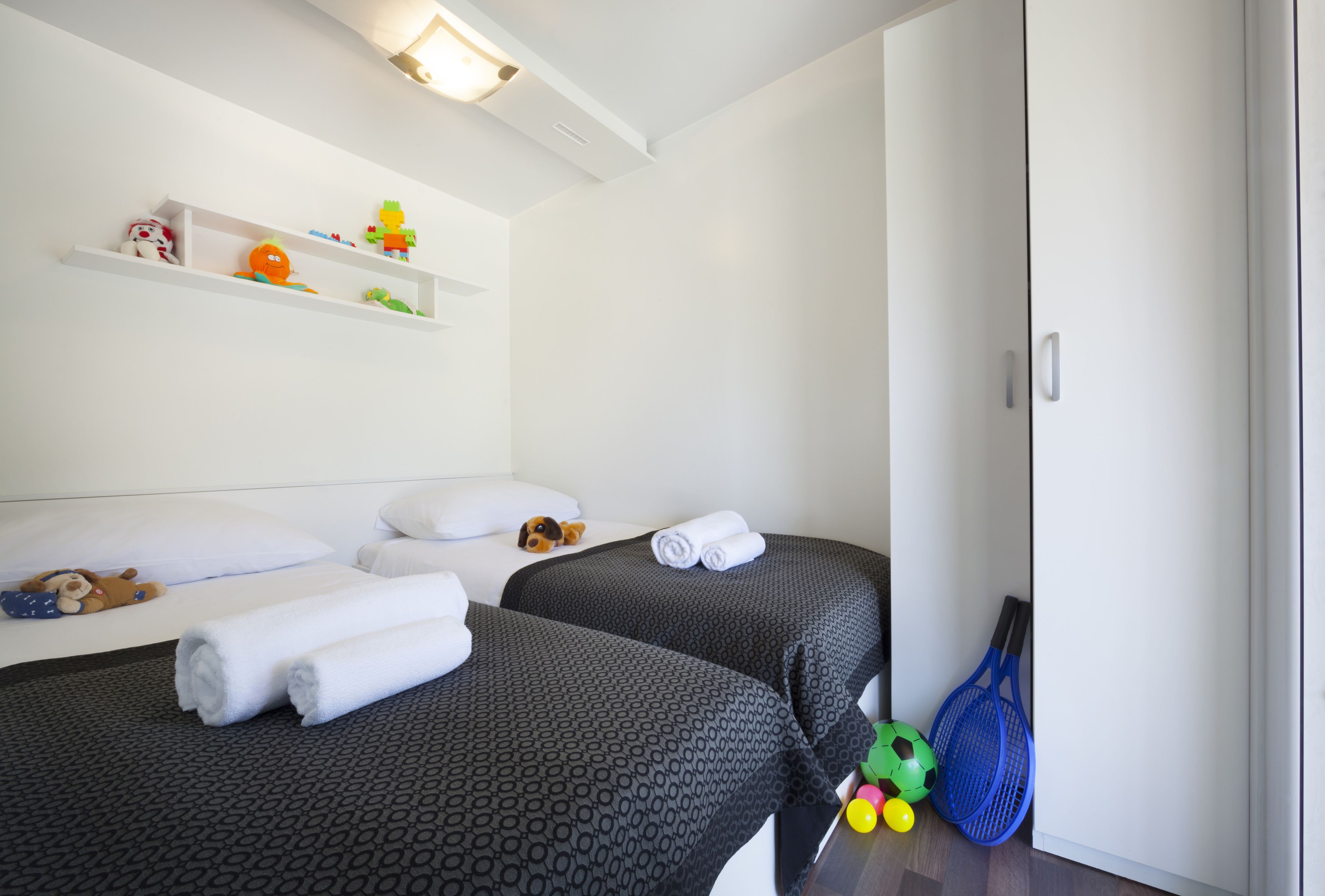Ein Hotelzimmer mit zwei Betten, einem Regal mit Spielzeug, einem Tennisracket und einer Tür.