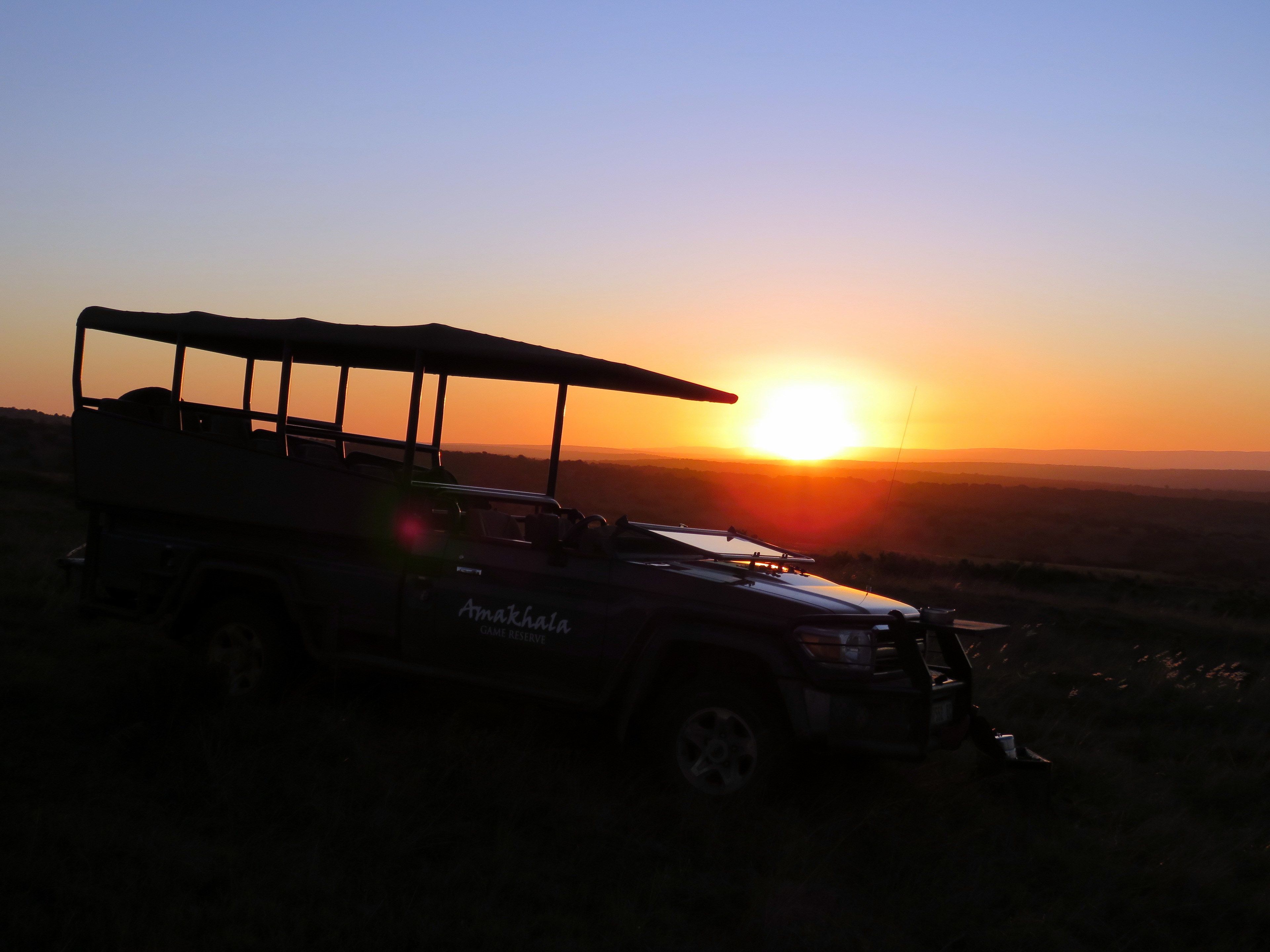Un vehículo safari con toldo estacionado en un campo césped durante el atardecer.
