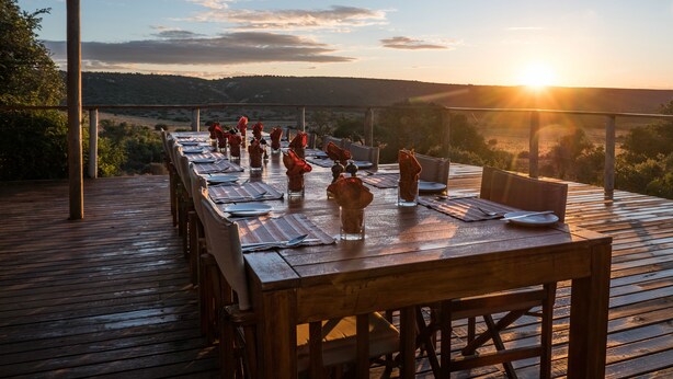 An outdoor dining area with a long wooden table set for a meal, overlooking a scenic landscape. - Woodbury Tented Camp - Amakhala Game Reserve (Sidbury)