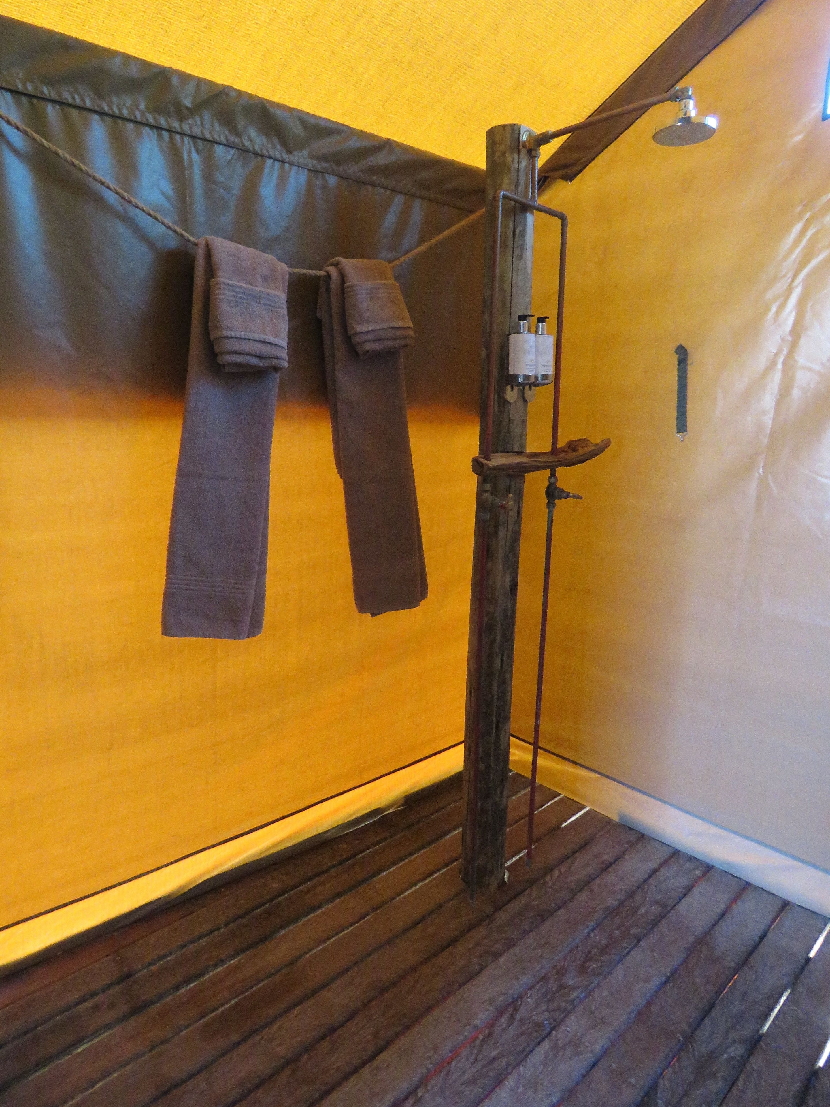 Ein Badezimmer mit Holzboden, einer Dusche inklusive Duschhandstück und Handtüchern an einem Halter.
