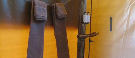 A bathroom with a wooden floor, a shower with a handheld showerhead, and towels hanging on a rack.