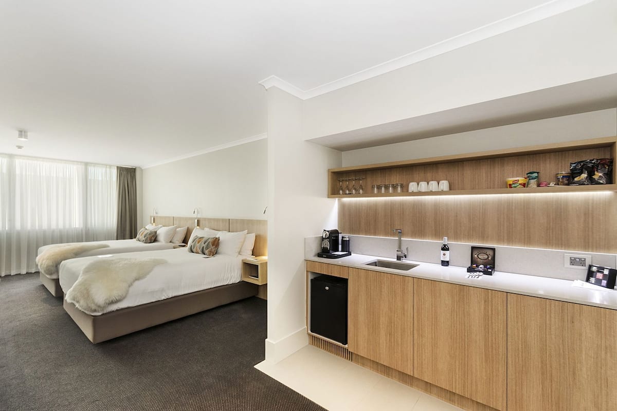 A hotel room with a bed, bedside tables, a built-in kitchen with a sink, and a small refrigerator.