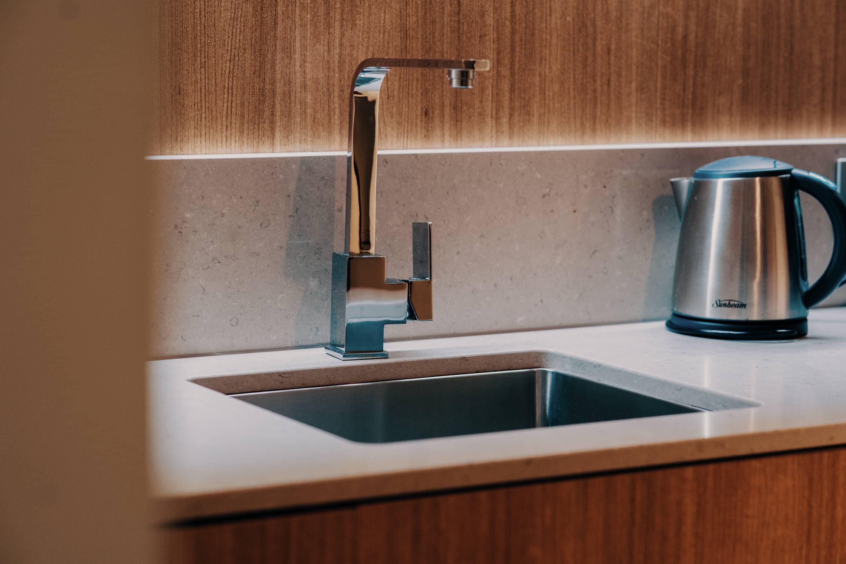 Eine moderne Küche mit Spüle aus Edelstahl, einer Armatur mit hohem Auslauf und einem Wasserkocher auf der Arbeitsfläche.