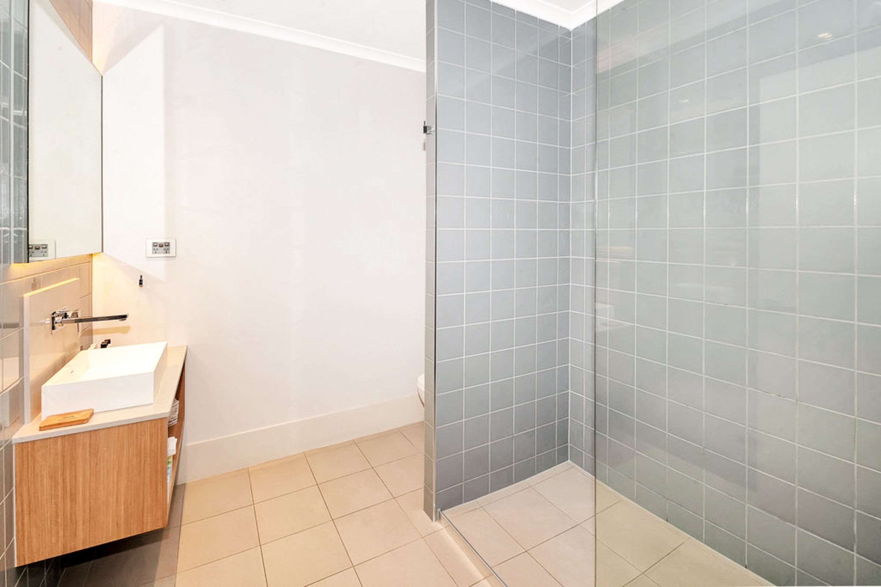Un bany modern amb una cabina de dutxa de vidre, un lavabo de fusta i un rentapelats blanc.