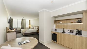 A modern hotel room with a separate dining area, a bed, a desk, and a small kitchen.