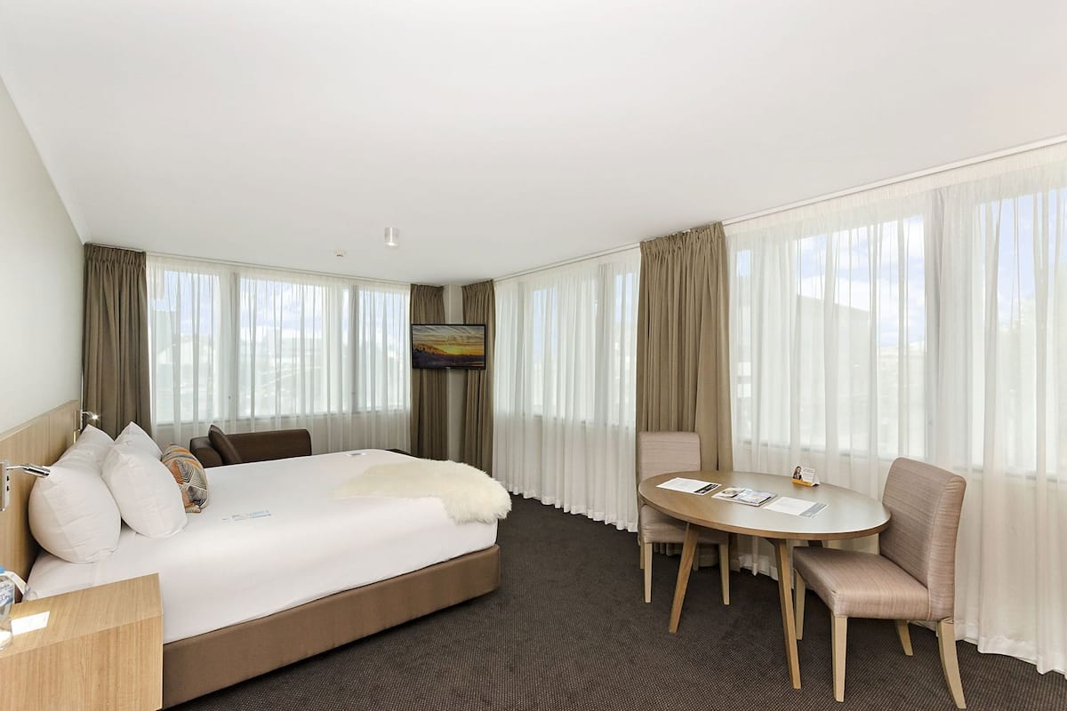 A hotel room with a bed, a desk, a chair, a round table, and a TV.