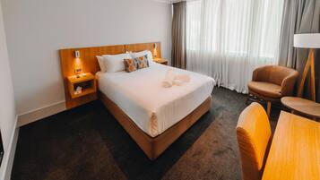 A hotel room with a large bed, a nightstand, a chair, a table, and a lamp.
