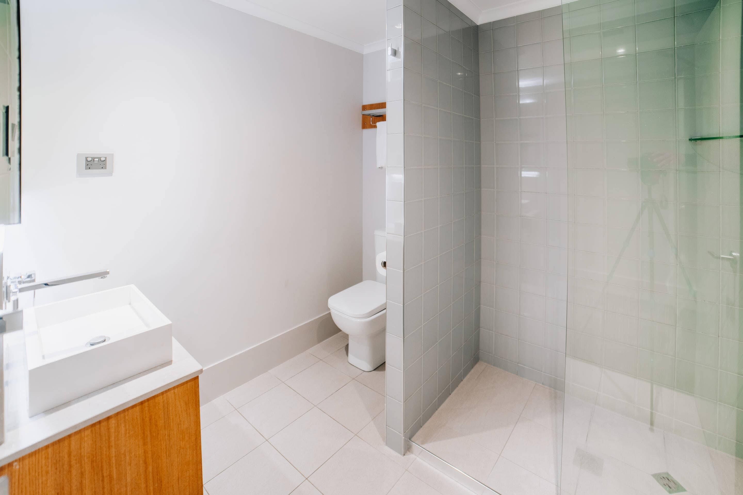 Un baño moderno con lavamanos blanco, inodoro y cabina de ducha con mampara de vidrio.