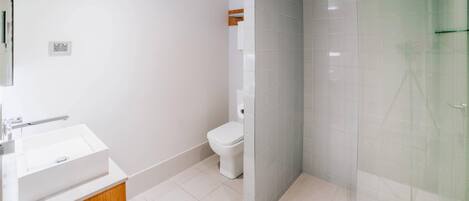 Un baño moderno con lavamanos blanco, inodoro y cabina de ducha con mampara de vidrio.