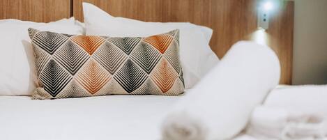 A neatly made bed with a patterned pillow and a rolled white towel.