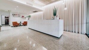 A modern reception area with a white reception desk, two orange chairs, a small table, and a potted plant. - Clarion Hotel Townsville (Townsville)