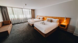 A hotel room with two beds, a sofa, a nightstand with a lamp, and a large window with curtains. - Clarion Hotel Townsville (Townsville)