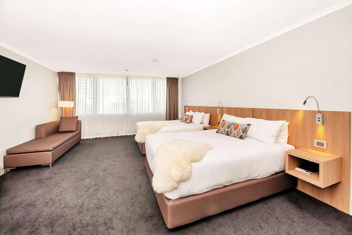 A hotel room with two beds, a sofa, a lamp, and a TV.