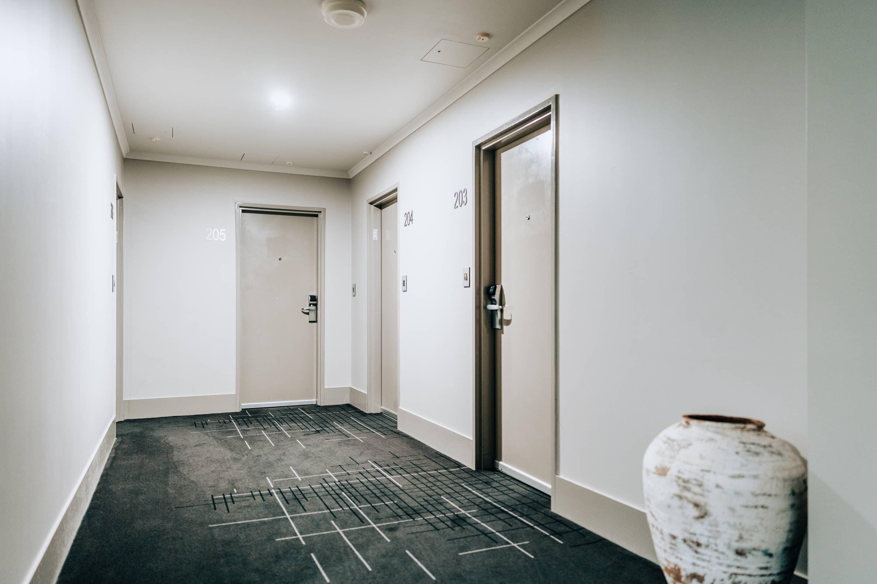 A hallway with carpeted flooring, numbered doors, and a white vase.