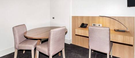 A small meeting room with a round table, two chairs, a desk with a telephone, and a wall-mounted TV.