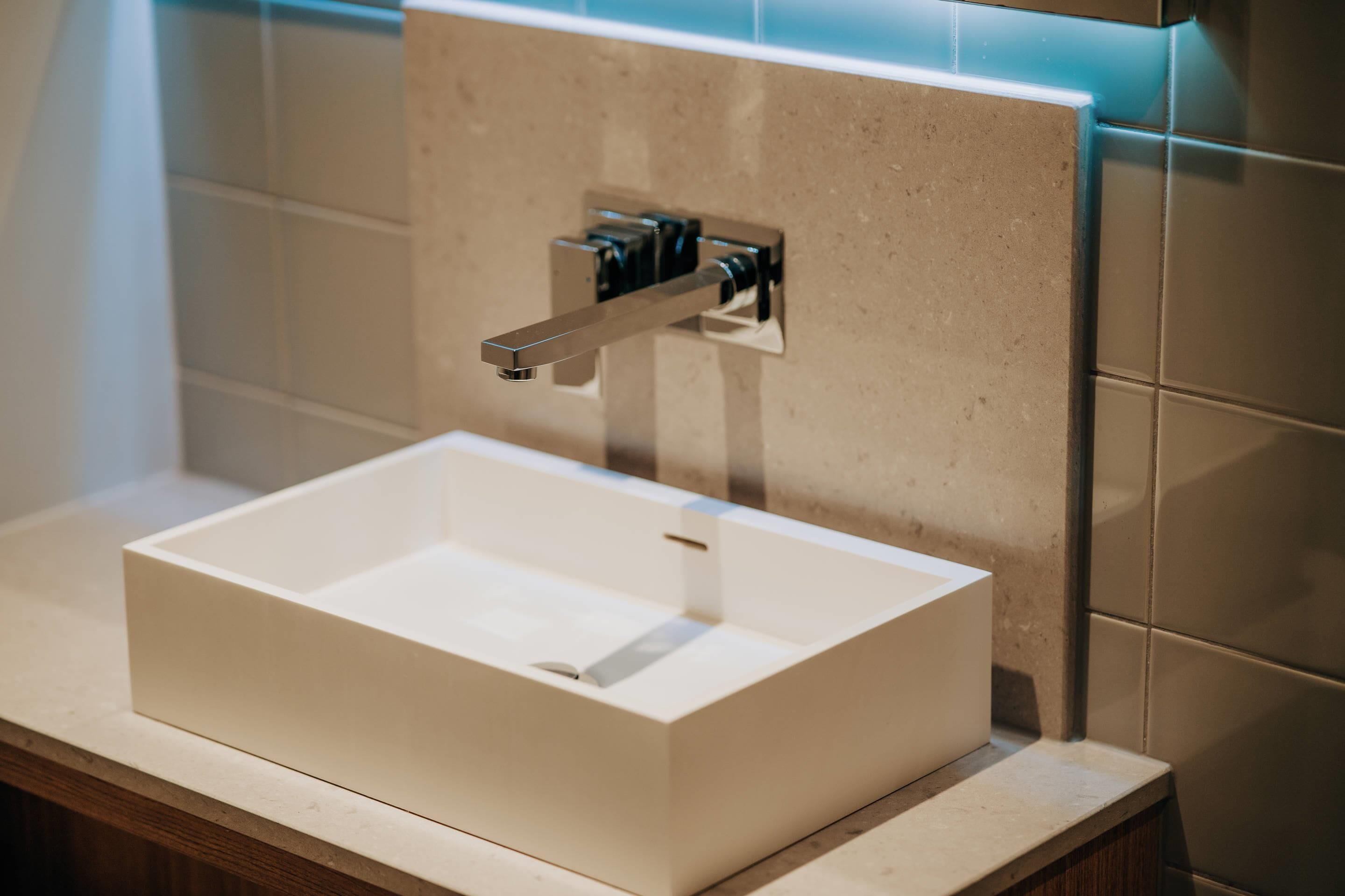A rectangular sink with a chrome faucet mounted on a beige tiled wall.