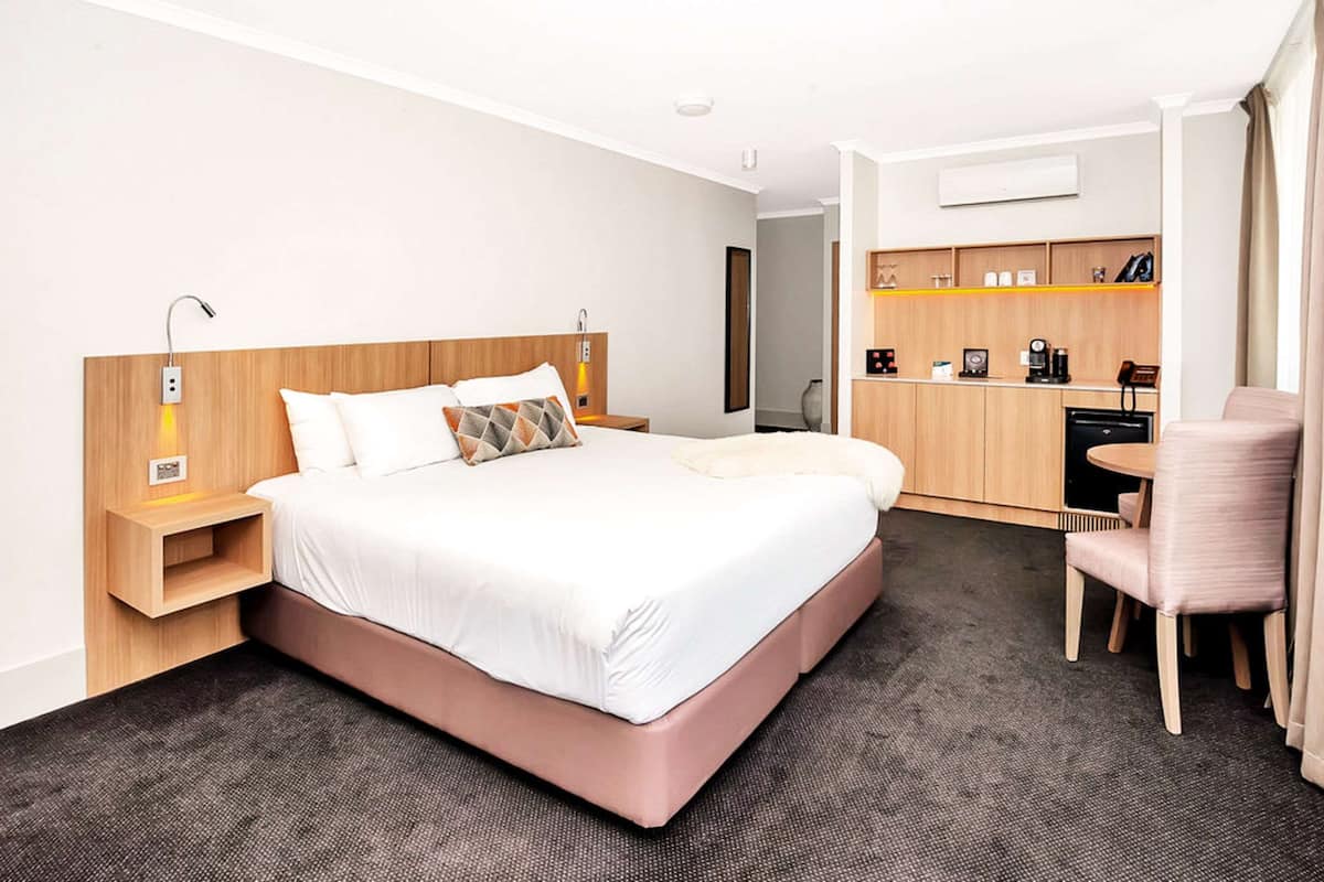 A modern hotel room with a large bed, bedside tables, a desk, and a chair.