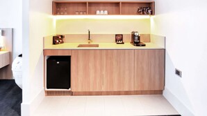 A compact kitchen with a built-in sink, wooden cabinets, and a countertop with a coffee machine and glassware. - Clarion Hotel Townsville (Townsville)