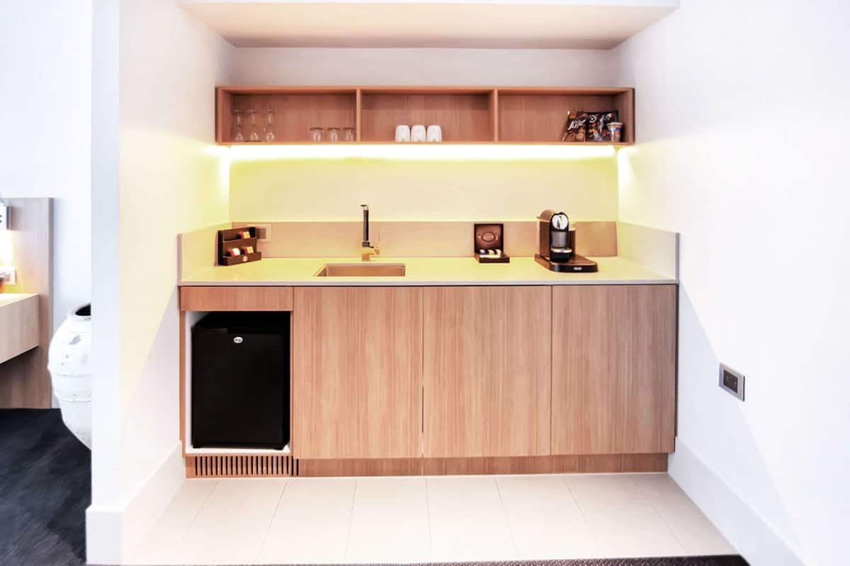 A compact kitchen with a built-in sink, wooden cabinets, and a countertop with a coffee machine and glassware.