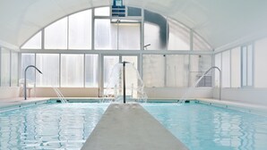 Une piscine intérieure de forme longue et étroite, dotée de grandes fenêtres et agrémentée d’un élément décoratif central avec de l’eau.