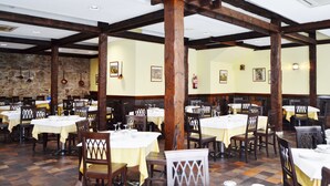 Un restaurant avec des poutres en bois, des murs en pierre et des tables dressées pour le repas.