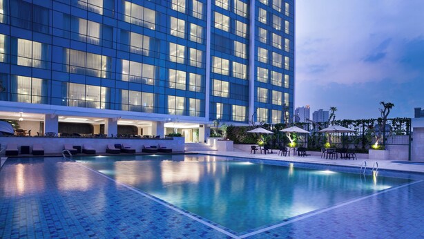 A swimming pool with lounge chairs and umbrellas, surrounded by a modern building with large windows. - Crowne Plaza Bandung by IHG (Bandung)