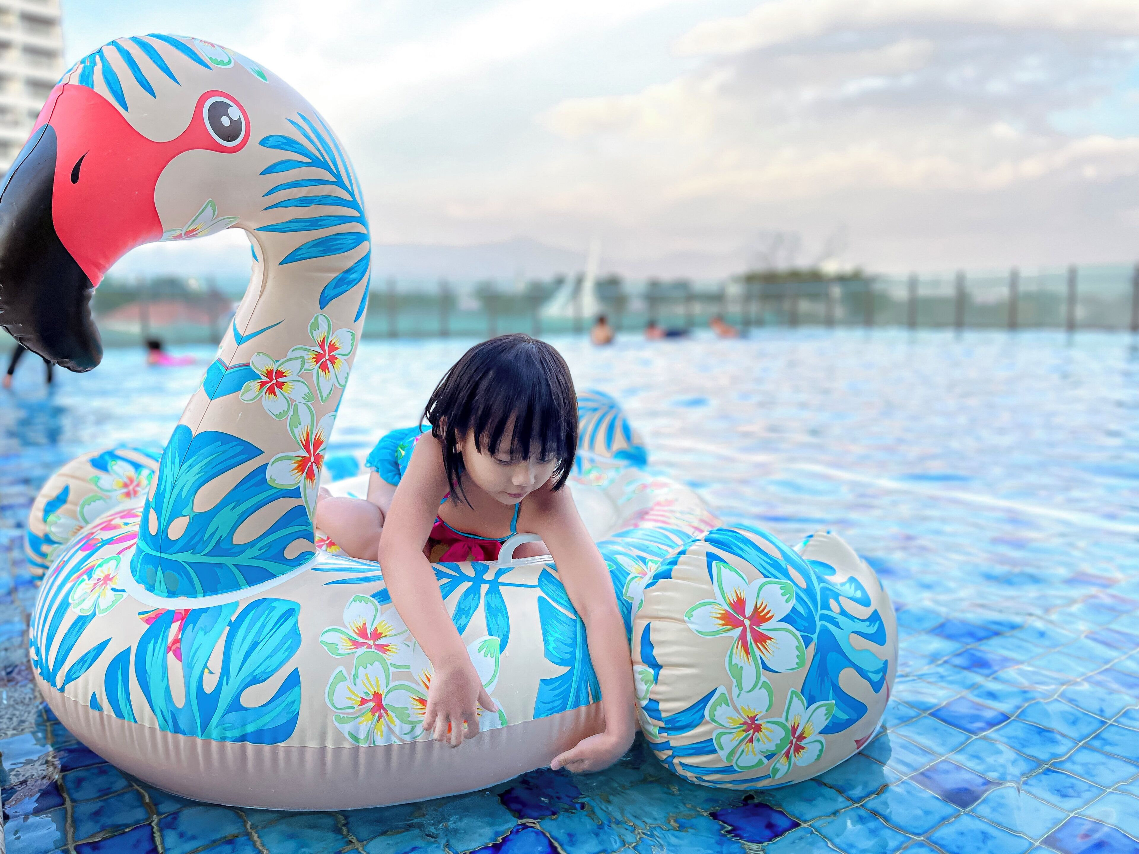 Un niño sobre un cisne inflable con motivos florales en una piscina.