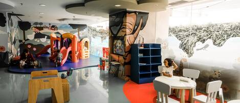 A children's play area with colorful play structures and a mural on the wall.