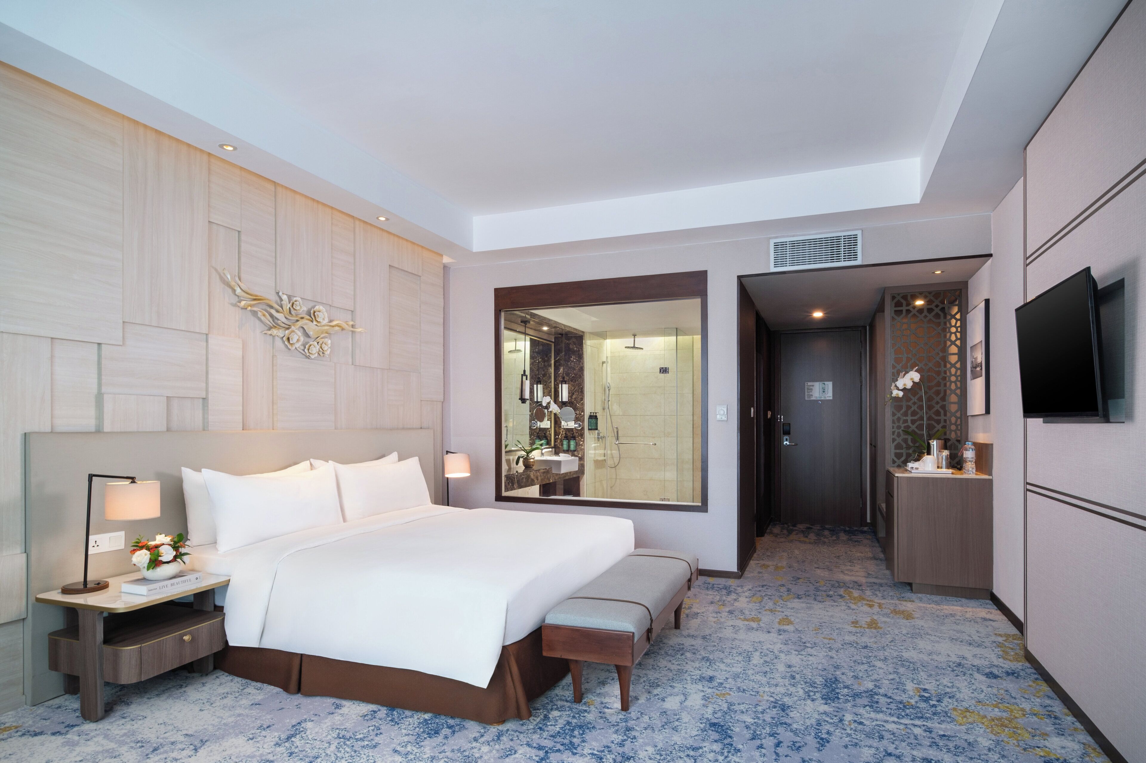 Een moderne hotelkamer met een groot bed, nachtkastjes, een spiegel, een televisie en een badkamer zichtbaar door een glazen deur.