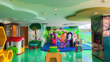 A children's play area with colorful play structures, a slide, and a mural of a farm scene.