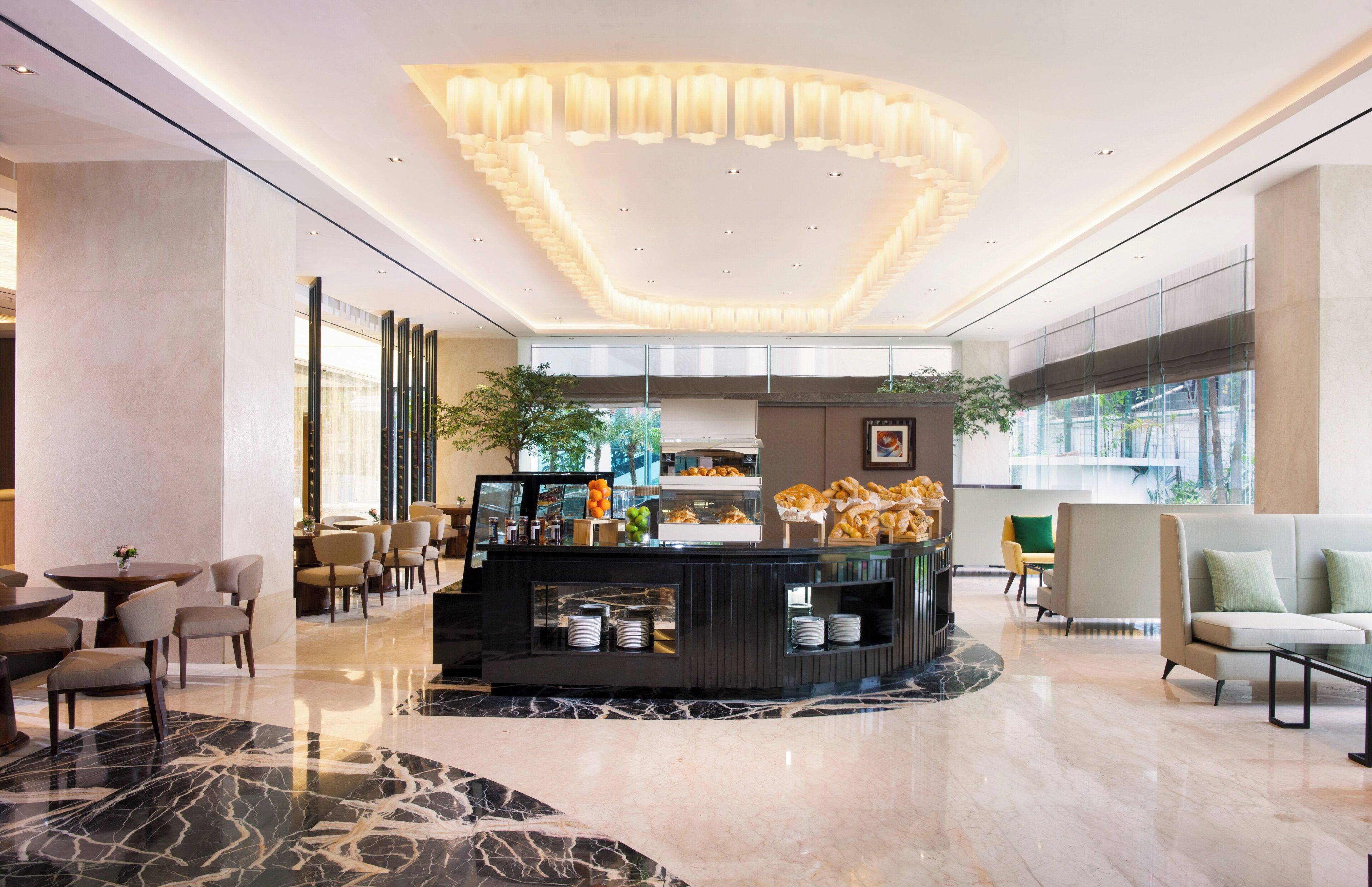 A modern hotel lobby with a marble floor, a central counter with food items, and seating arrangements.