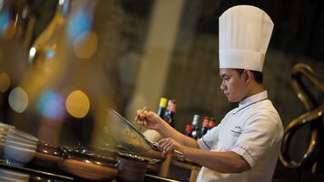 A chef in a white uniform and hat, preparing food at a kitchen counter with various cooking utensils and ingredients.
