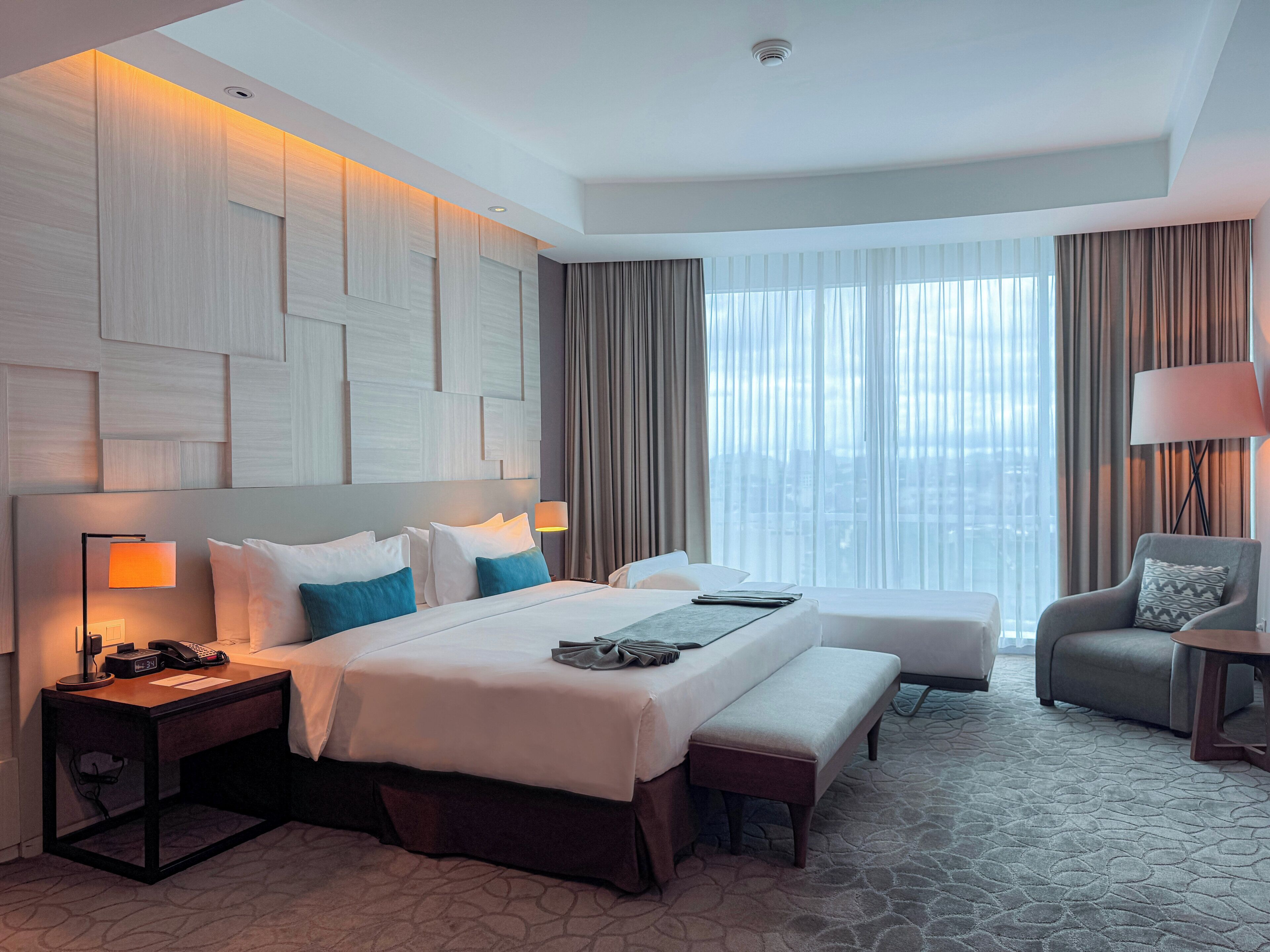 A hotel room with a large bed, a desk, a chair, and a view of the city.
