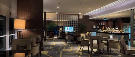 A hotel lobby with a bar area, seating arrangements, and a television screen.