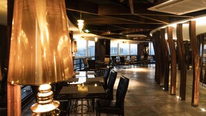 A restaurant with high tables and chairs, a large copper lamp, and a view of the city through large windows. - Crowne Plaza Bandung by IHG (Bandung)