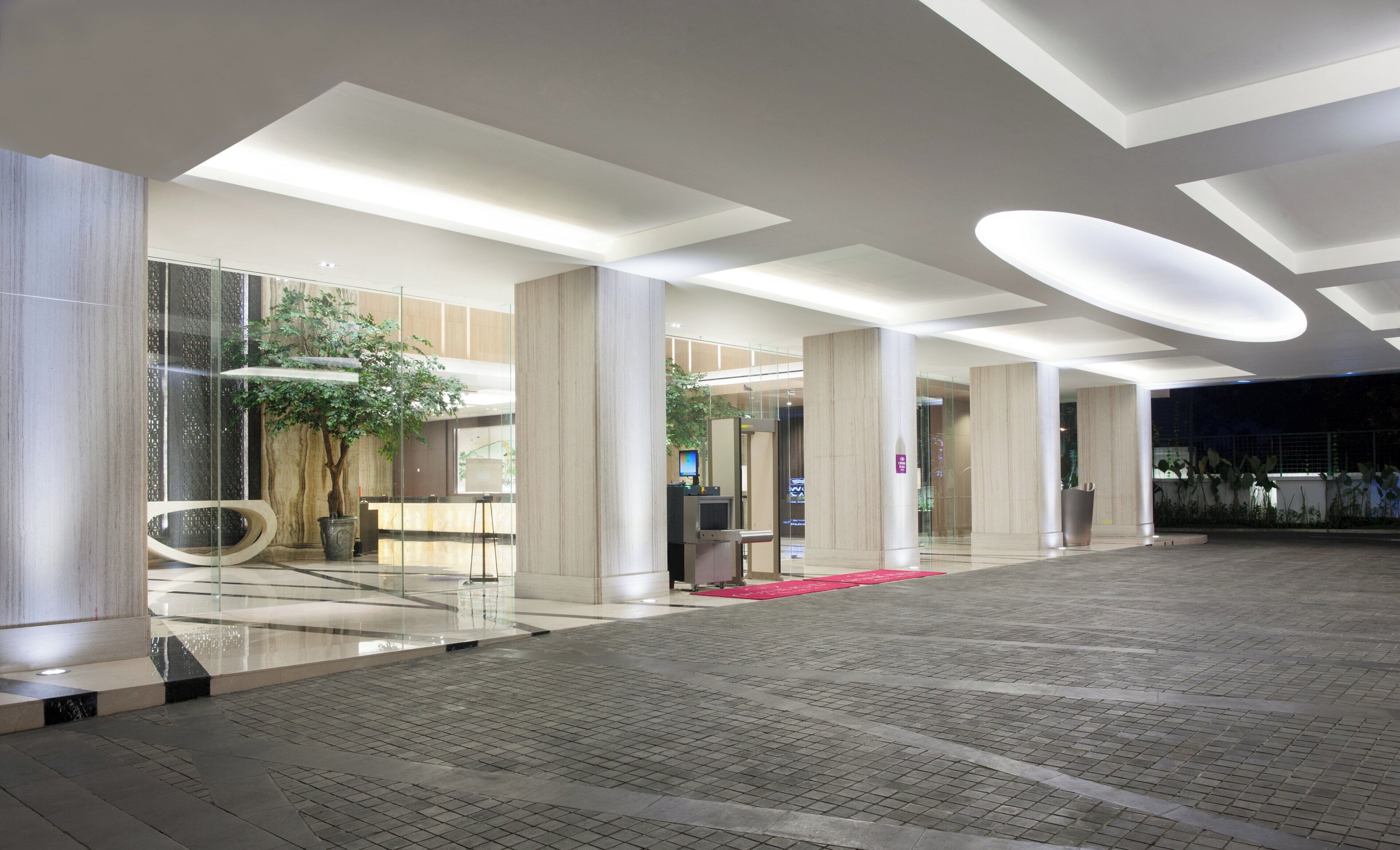 Een moderne lobby met een glazen gevel, een receptiebalie en een rode loper naar de ingang.