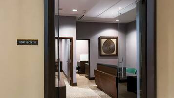 A hotel reception area with a glass partition, a reception desk, a seating area, and a wall-mounted artwork.