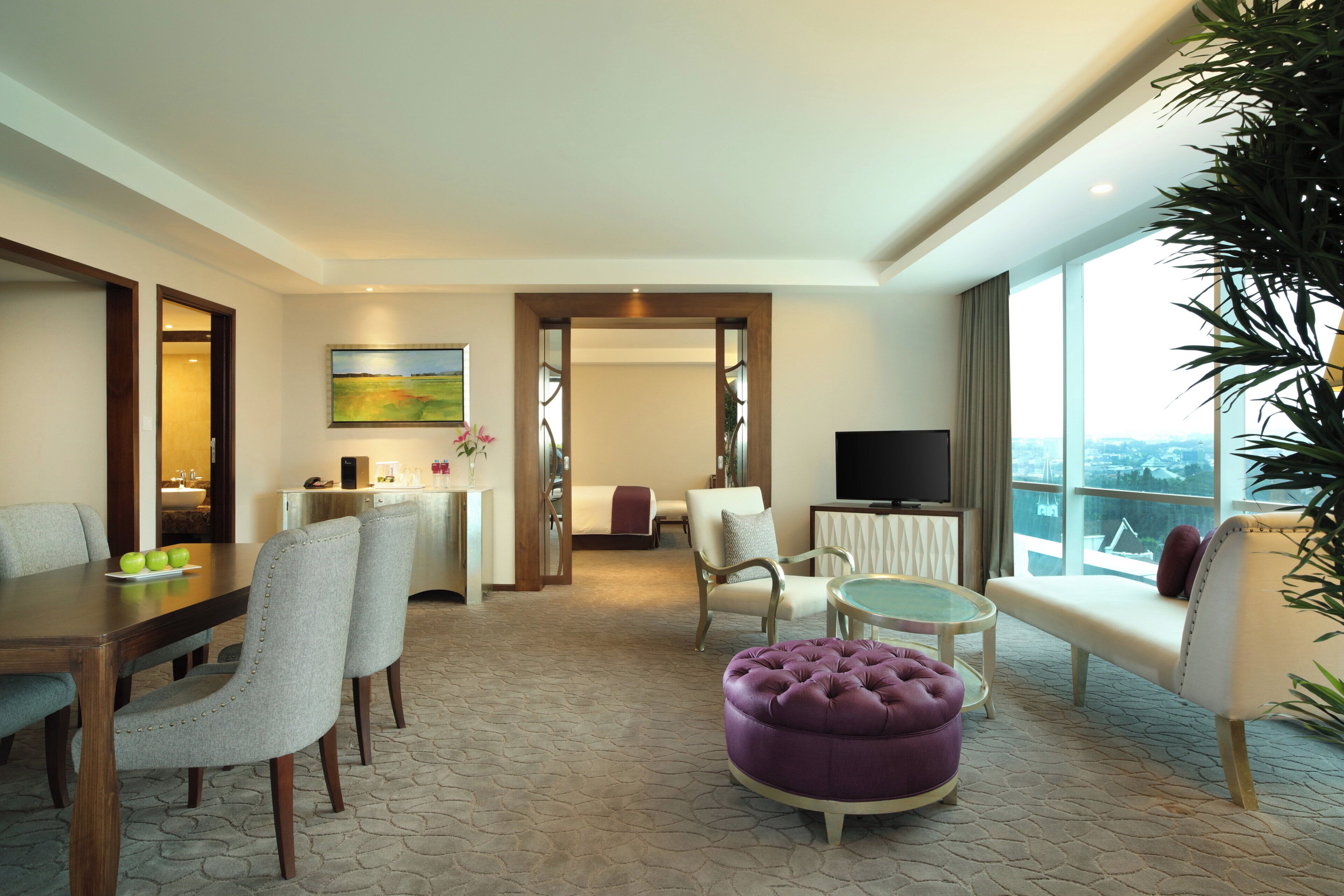 A hotel room with a dining area, a sofa, a television, and a large window with a view.