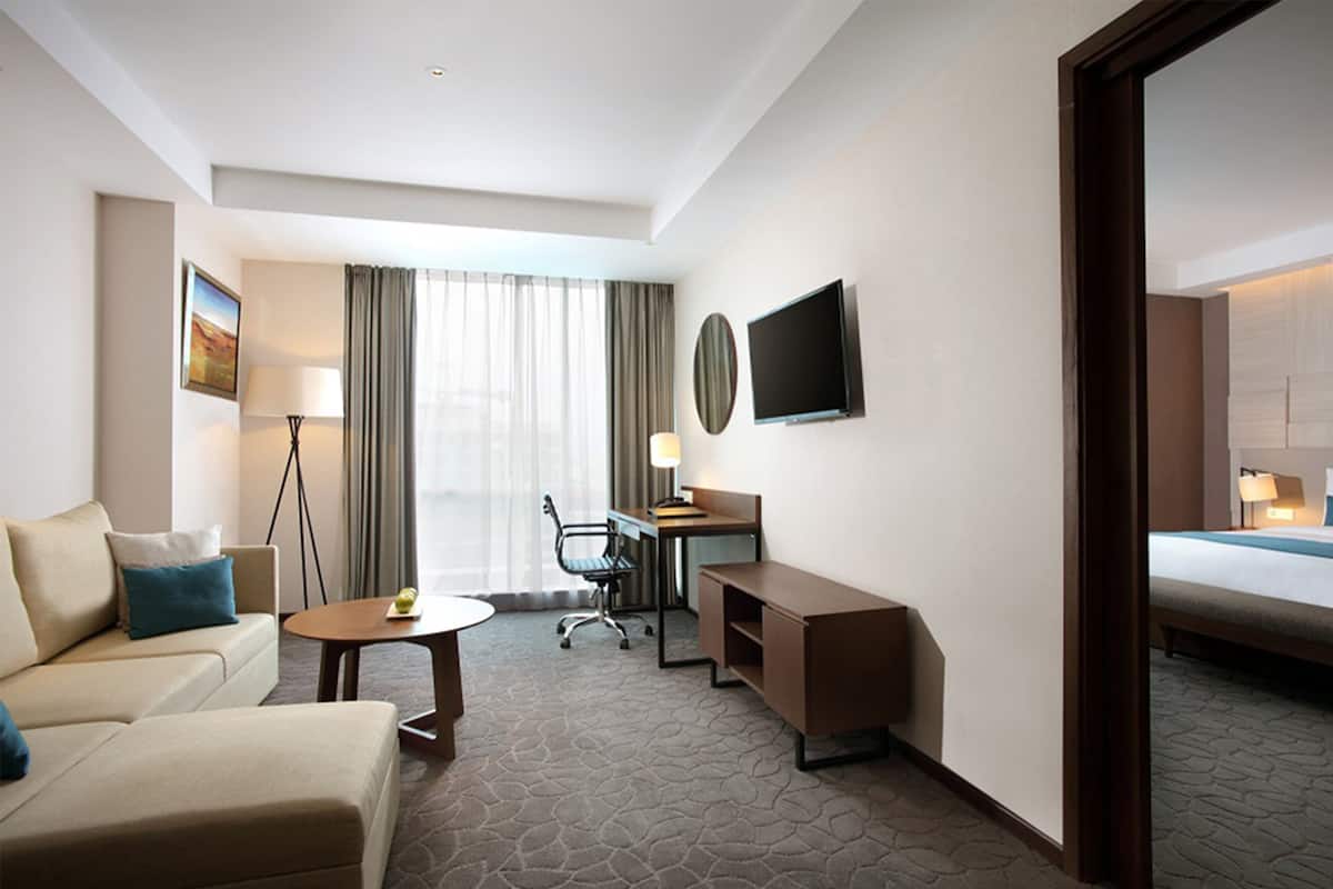A hotel room with a bed, a desk, a chair, a sofa, a small table, and a TV.