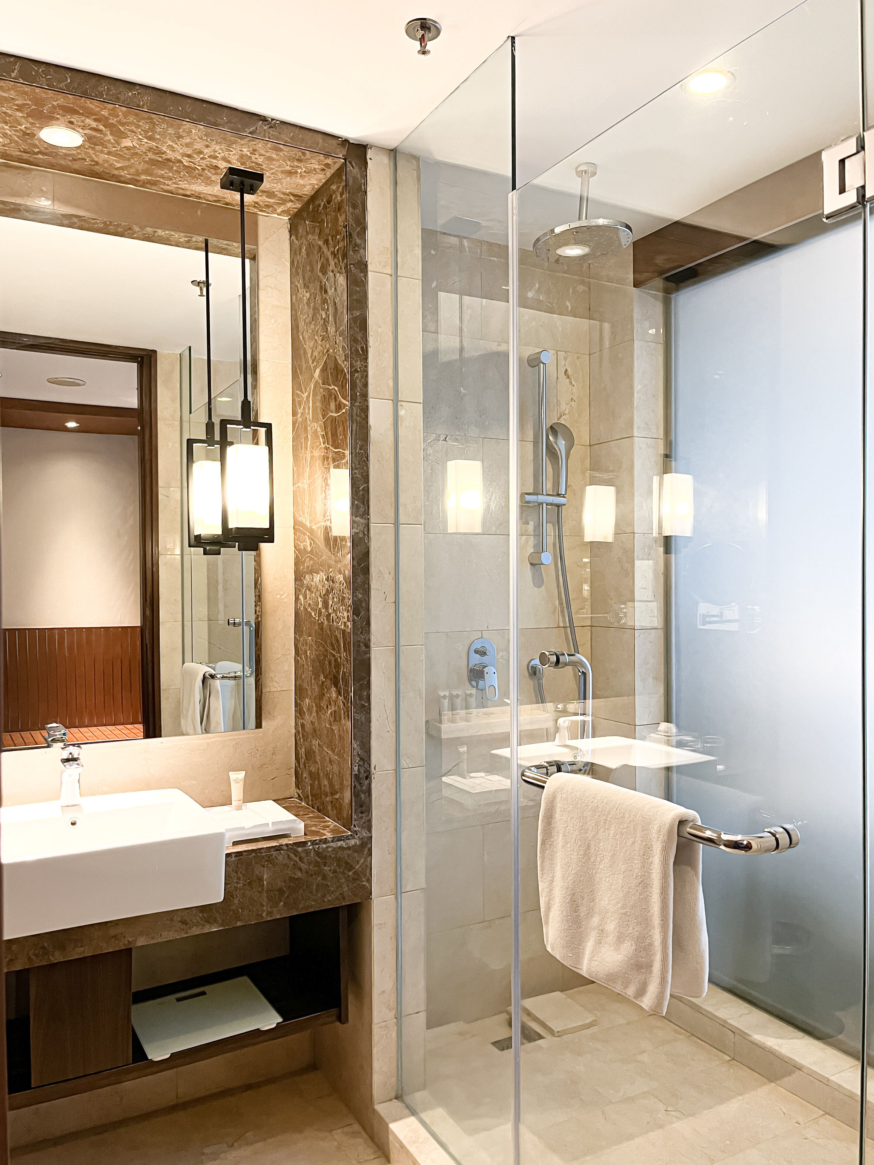 Une salle de bain moderne dotée d’une douche à parois de verre, d’un grand miroir et d’un meuble-lavabo avec un évier et un porte-serviettes.