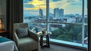 A hotel room with a large window offering a city view at sunset. - Crowne Plaza Bandung by IHG (Bandung)