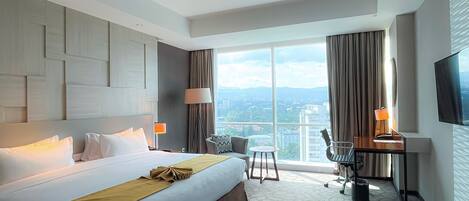 A hotel room with a large bed, a desk, a chair, and a TV.